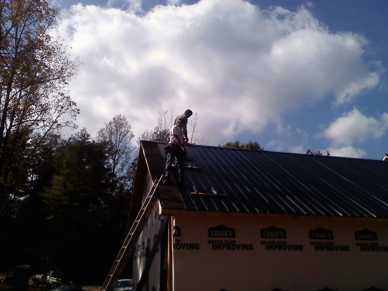 Roofer fastening dark metal panels high against a cloudy sky, from a Roof Inspection job in Bowen
