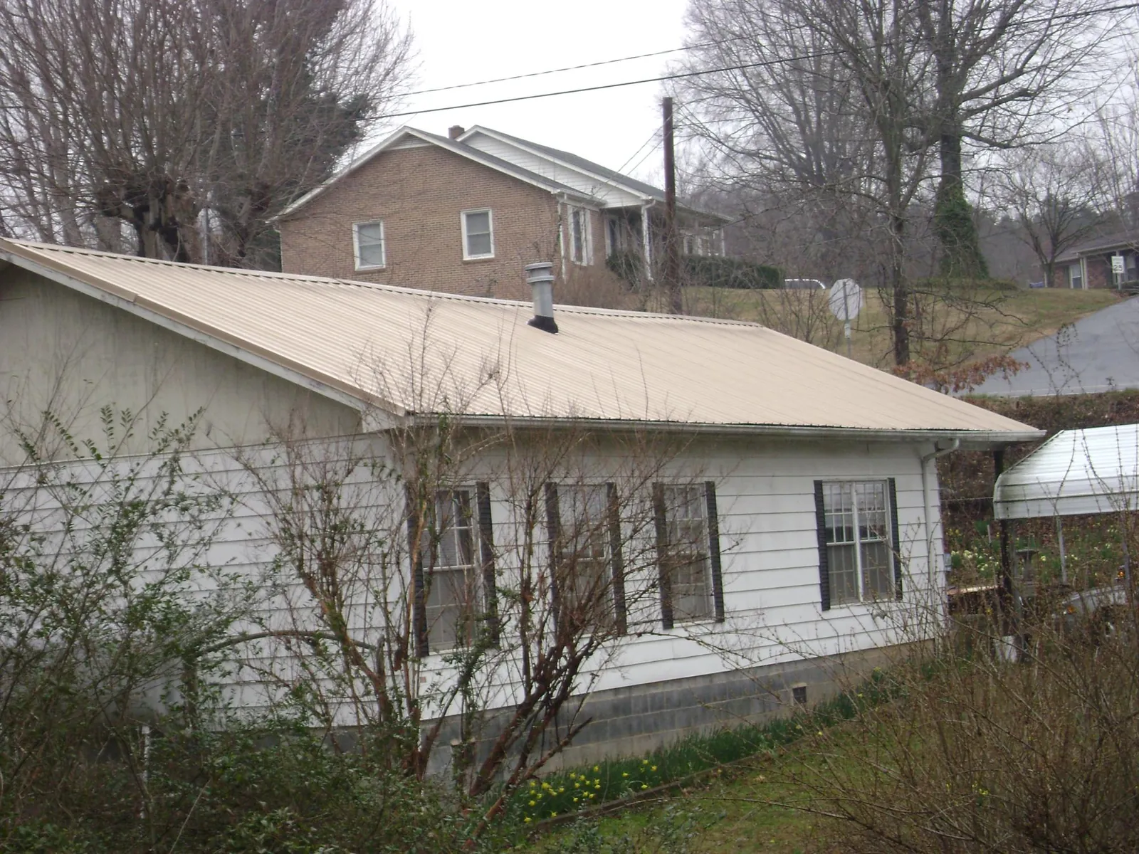 Tan metal roof on a white sided house set into a hillside — Commercial Roofing by Roofing Brothers in Bowen