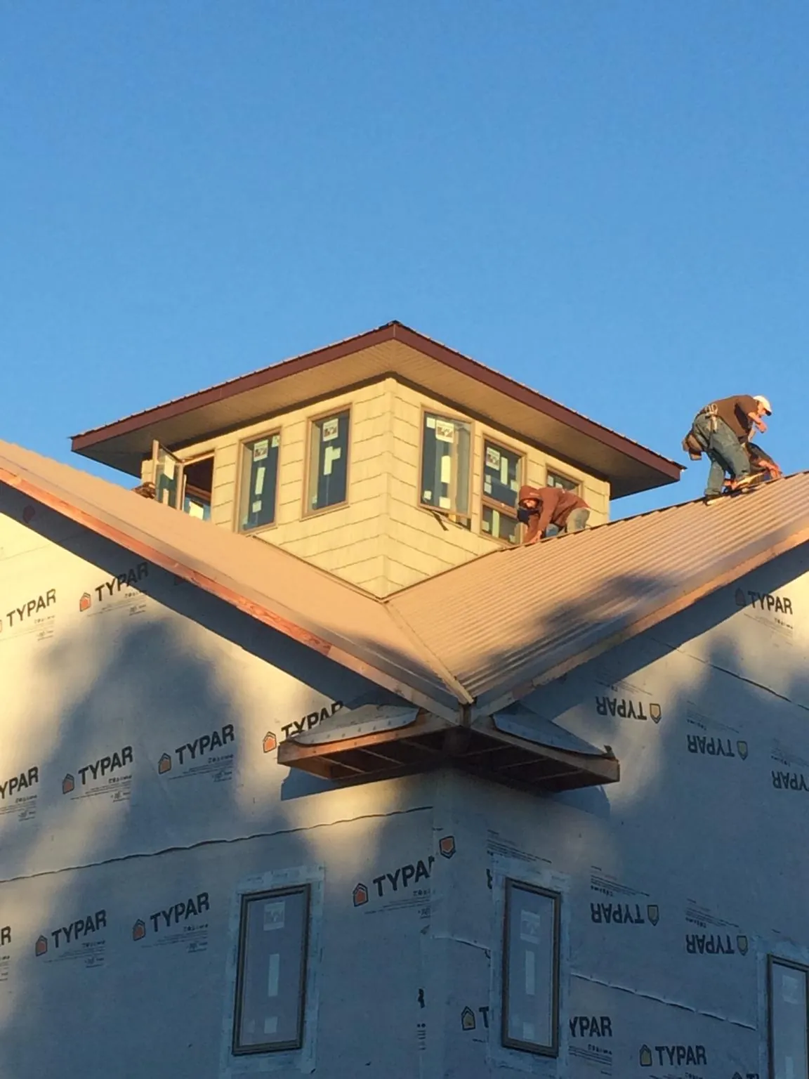 Roofers working around a rooftop cupola on a new metal roof at sunset — Roof Waterproofing in Bowen by Roofing Brothers